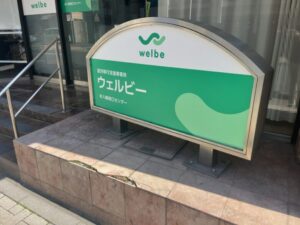 就労移行支援事業所「ウェルビー 本八幡南口センター」の屋外看板アップ。welbeロゴと「ウェルビー」「本八幡南口センター」の表記（2026年3月5日筆者撮影）