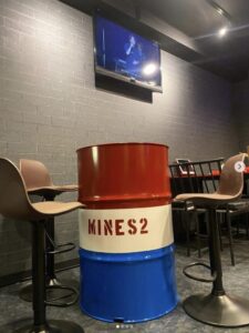 マインズ2 行徳店内の様子 ドラム缶テーブルとモニターがある客席空間