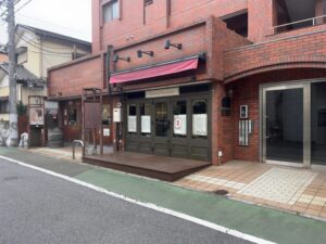ロステリア・ディ・トシの店舗外観。市川市新田の通り沿いにあるレンガ調の建物と入口まわり（2026年3月筆者撮影）