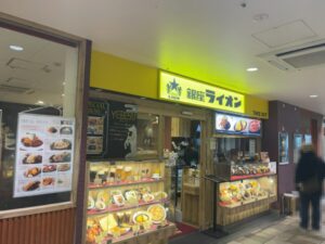 シャポー本八幡の銀座ライオン シャポー本八幡店の外観。黄色い看板と店頭のメニュー・ショーケースが見える（2026年3月17日筆者撮影）