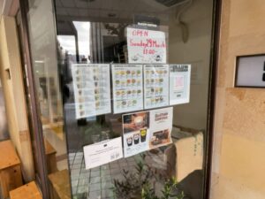 DeCUP COFFEE 市川店の店頭に掲示された3月29日11時オープンのお知らせとメニュー(2026年3月28日筆者撮影)