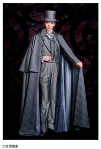 宝塚歌劇花組全国ツアー公演『マジシャンの憂鬱』の舞台衣装を着た出演者ビジュアル。シルクハットとロングコート姿で立つ人物の写真。