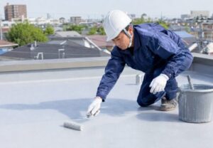 屋上で作業員がローラーを使って防水塗装を行っている防水工事のイメージ